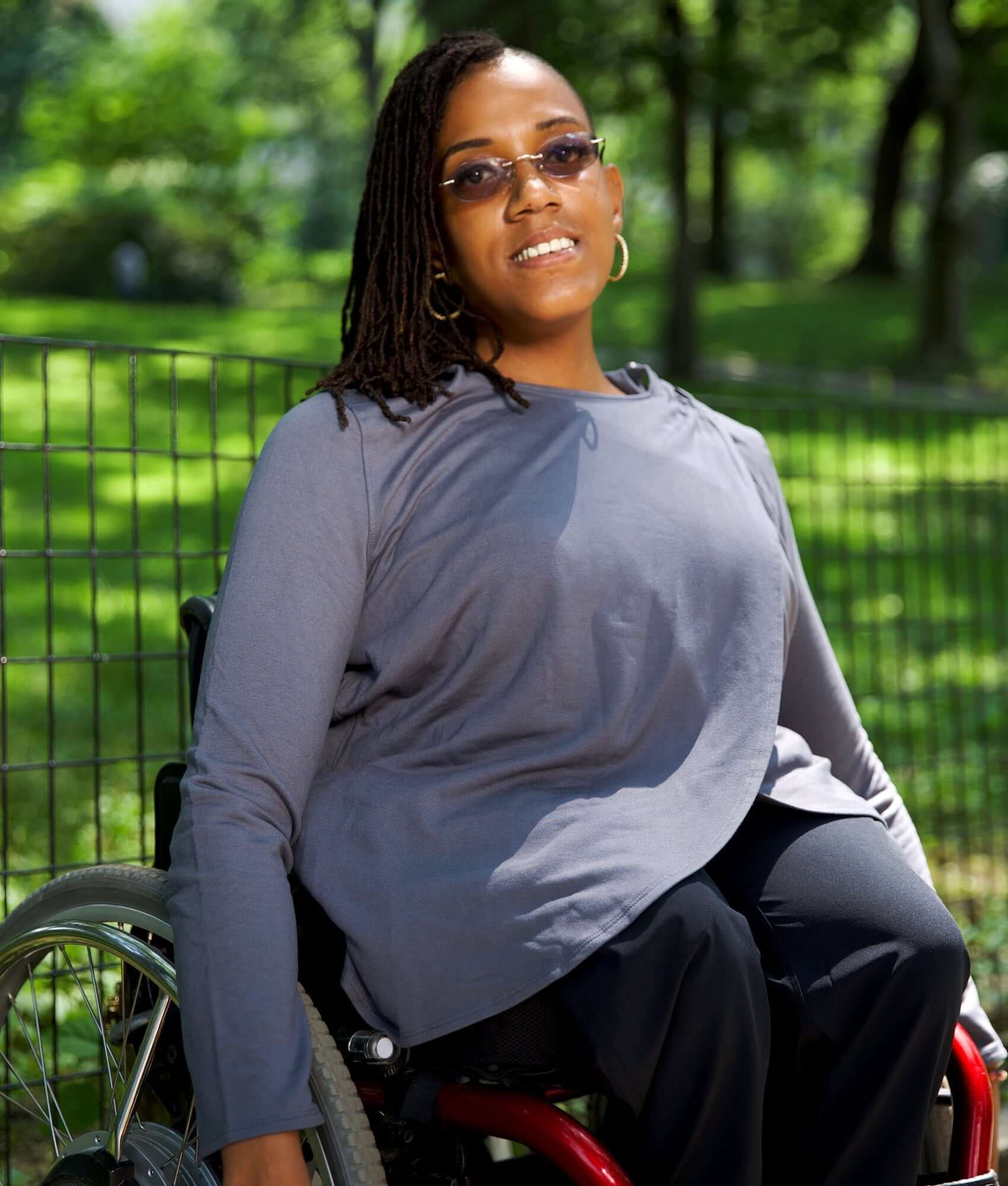 Woman in a wheelchair wearing a women's adaptive hooded wrap cardigan in a sunny park setting.