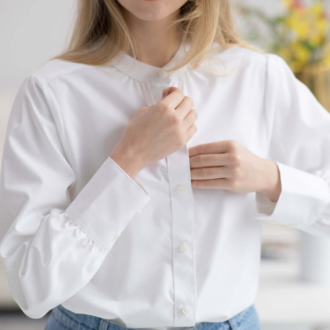 Close-up of a woman fastening buttons on a women's adaptive classic white blouse with a modern design.