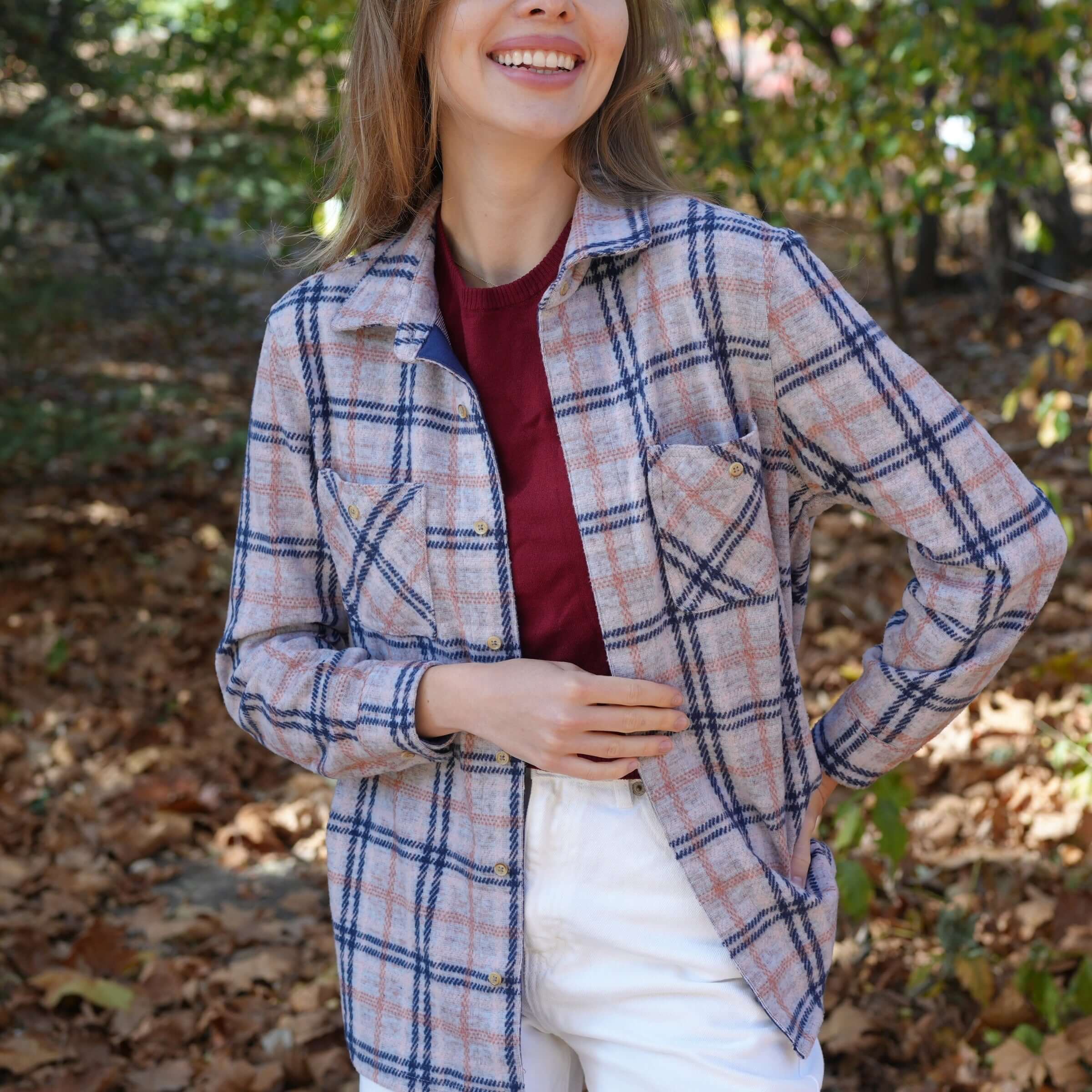 Women wearing a pink, navy, and gray plaid flannel shirt outdoors amidst autumn leaves.